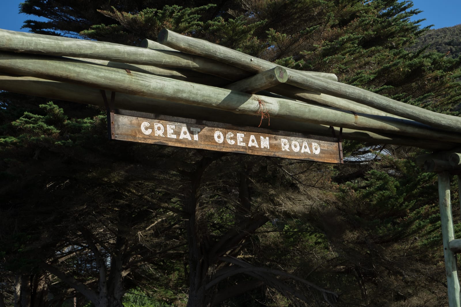 A wooden arch with a sign reading Great Ocean Road, framed by dark cypress trees