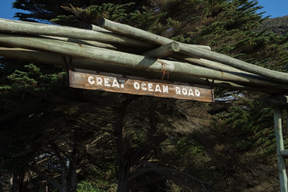 A wooden arch with a sign reading Great Ocean Road, framed by dark cypress trees
