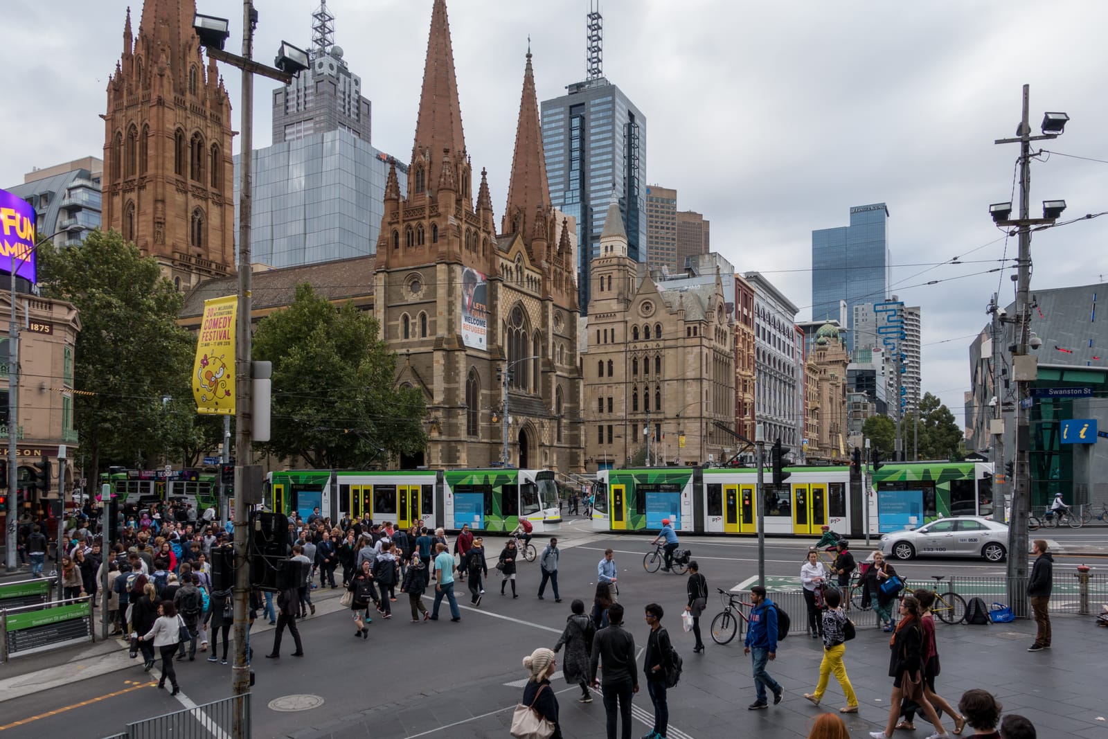 The spires of St Paul's Cathedral above a busy Melbourne intersection with green trams and crowds