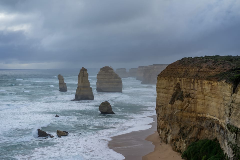 Limestone stacks standing in a grey, churning sea below tall cliffs, under heavy cloud